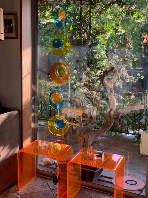 Groovy clear color plexiglass hanging vertical art mobile by AtomicMobiles.com with mod lucite tables in front of beautiful large floor to ceiling window with view of trees and garden - AtomicMobiles.com