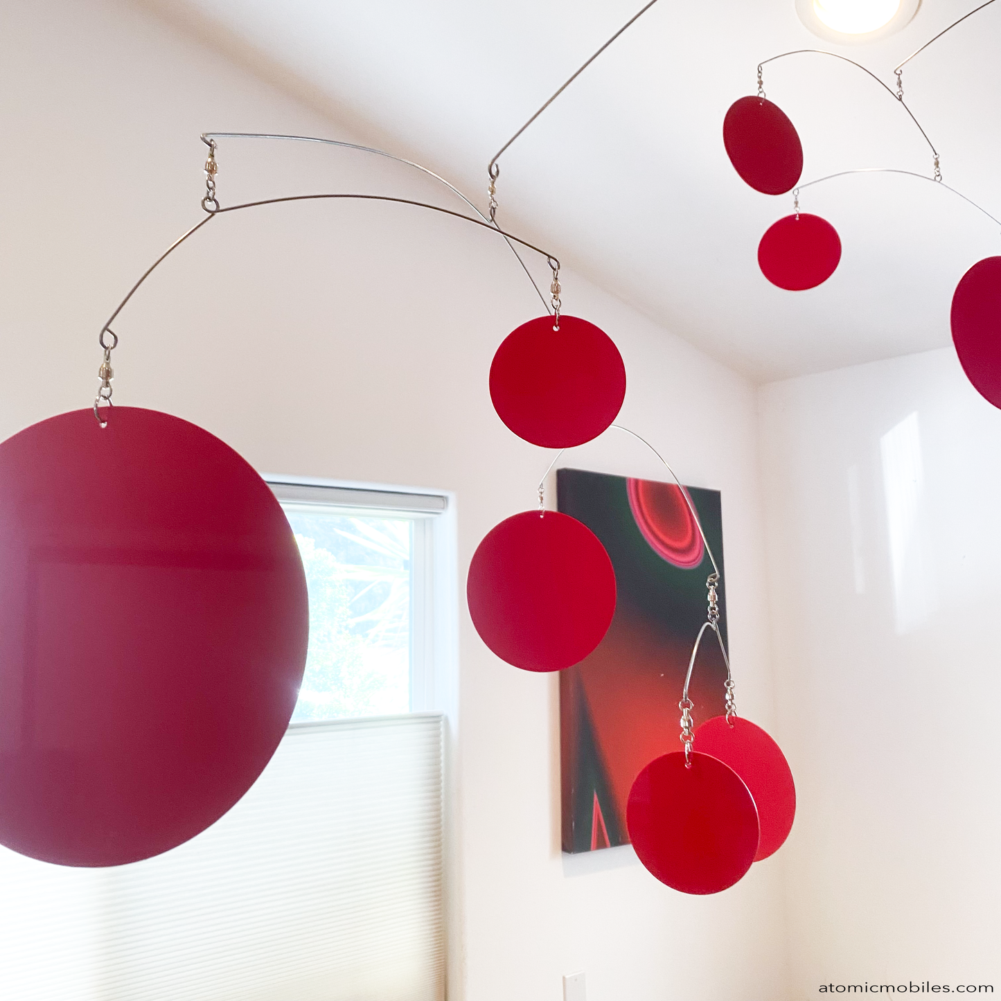 Closeup of XL Red Kinetic Hanging Art Mobile by AtomicMobiles.com - large red circles in large mobile in dining room over wood table with abstract art in background made in Los Angeles