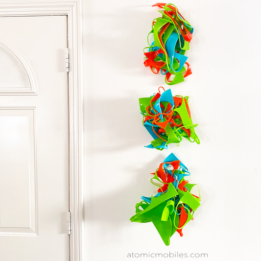 Colorful 3D wall art hanging next to front door in a vertical row in Lime Green, Aqua Blue, and Orange - recycled acrylic abstract 3D wall art by AtomicMobiles.com