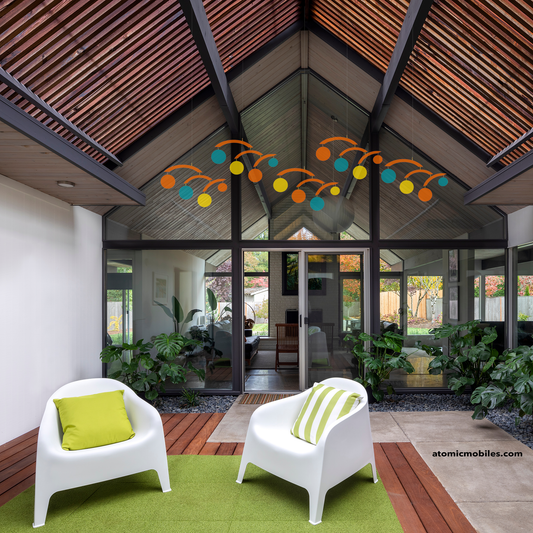 5 Jetsetter hanging art mobiles in Palm Springs colors of transparent orange, teal, and yellow in atrium of beautiful modern Eichler home with white chairs and plants -- mobiles by AtomicMobiles.com