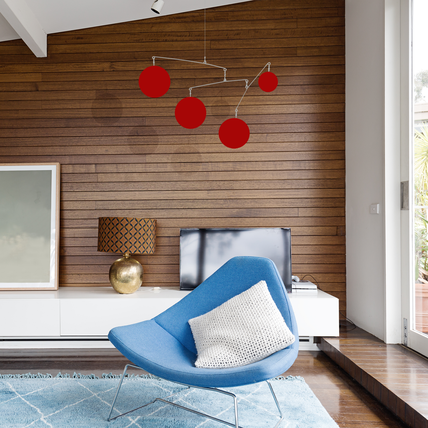 Mid century modern living room with blue chair, wood paneled wall, and red Jetsetter XL kinetic hanging art mobile by AtomicMobiles.com