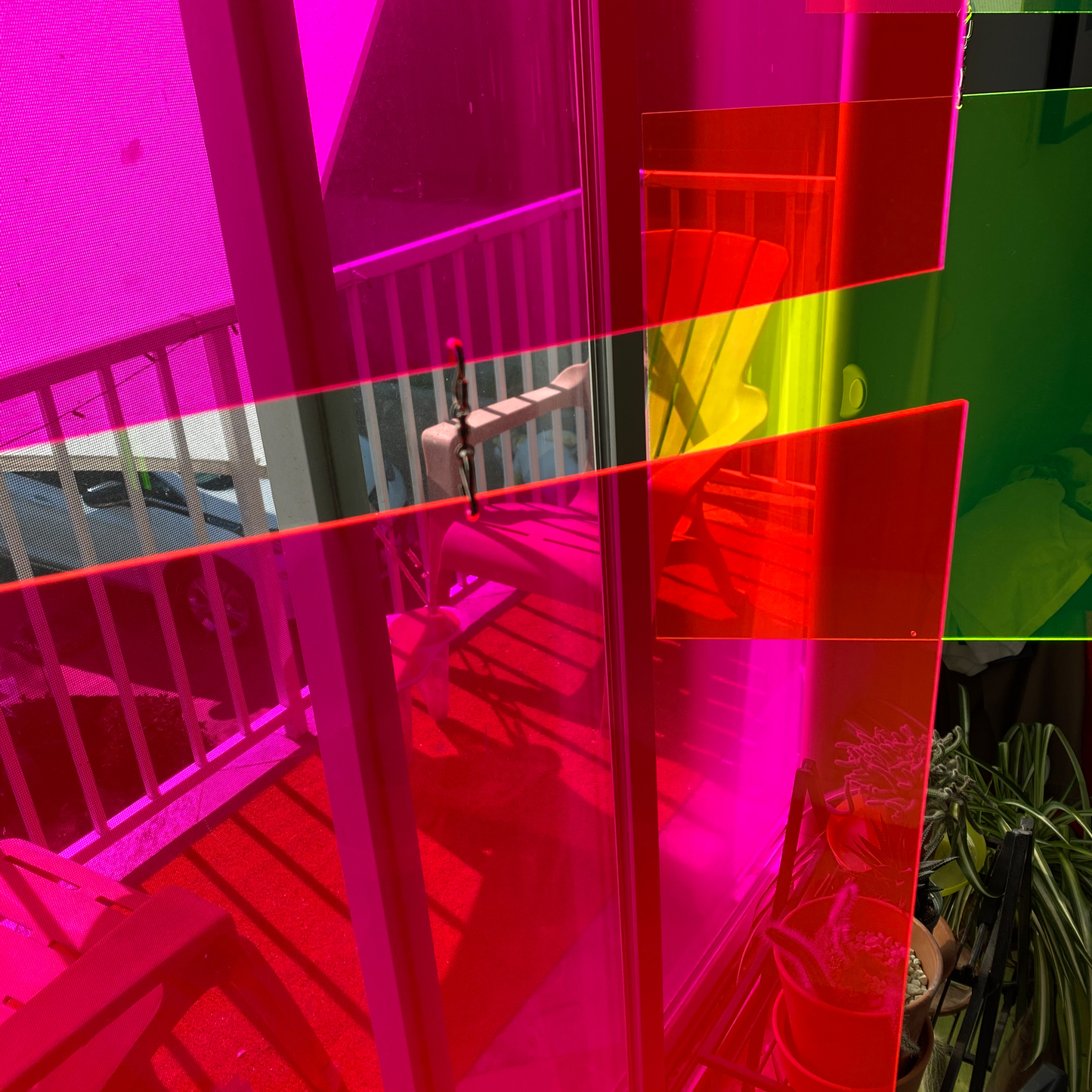 Neon Fluorescent Pink and Neon Fluorescent Green kinetic art mobiles by AtomicMobiles.com with plants and balcony through patio doors