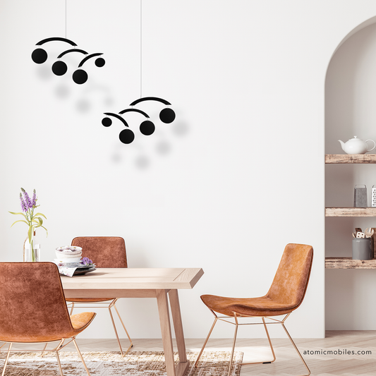 Dining room with wooden table and chairs, wall decors, and a shelf with 2 black Modernist hanging kinetic art mobiles by AtomicMobiles.com