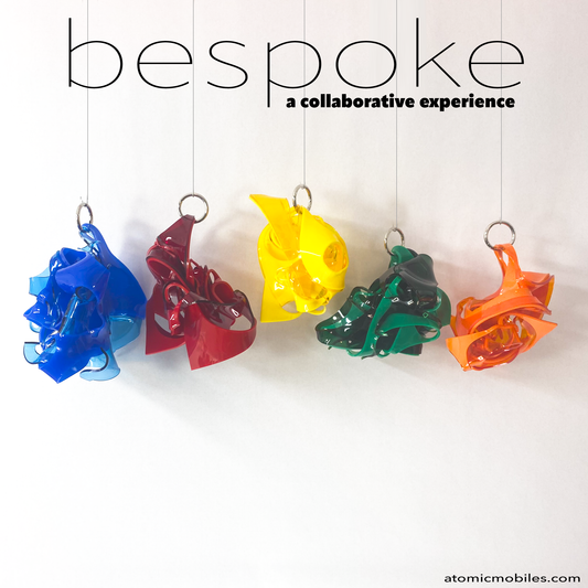 Five colorful mobiles hanging against a white background with 'bespoke' text above. Bespoke is a collaborative experience, multi color art sculpture shown in blue, yellow, orange, red, and green . You choose your colors for this modern plexiglass art by AtomicMobiles.com
