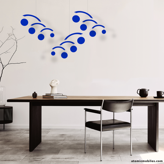 The Modernist Mobiles in opaque navy blue in a group of 3 hanging over a long contemporary dining table with leather chair and tea pot - kinetic modern hanging art mobiles by AtomicMobiles.com