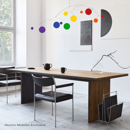 Lovely Rainbow LGBTQ+ Pride kinetic hanging art mobile in modern dining room with abstract art on wall and leather chairs. Pride mobile by AtomicMobiles.com