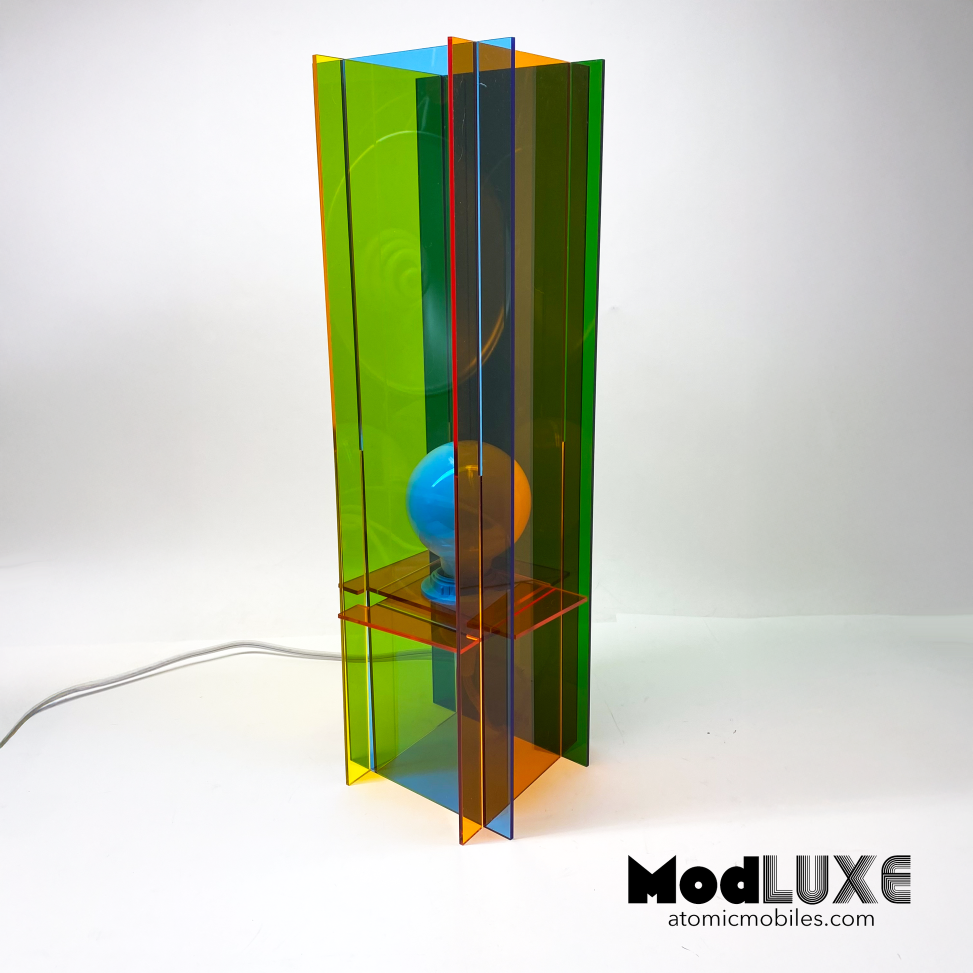 Back view of ModLUXE Space Age Lamp in groovy 1970s style and plexiglass acrylic colors of transparent orange, blue, green, and yellow. Colorful lamp with a transparent design on a white background, featuring the brand 'ModLUXE' by AtomicMobiles.com.
