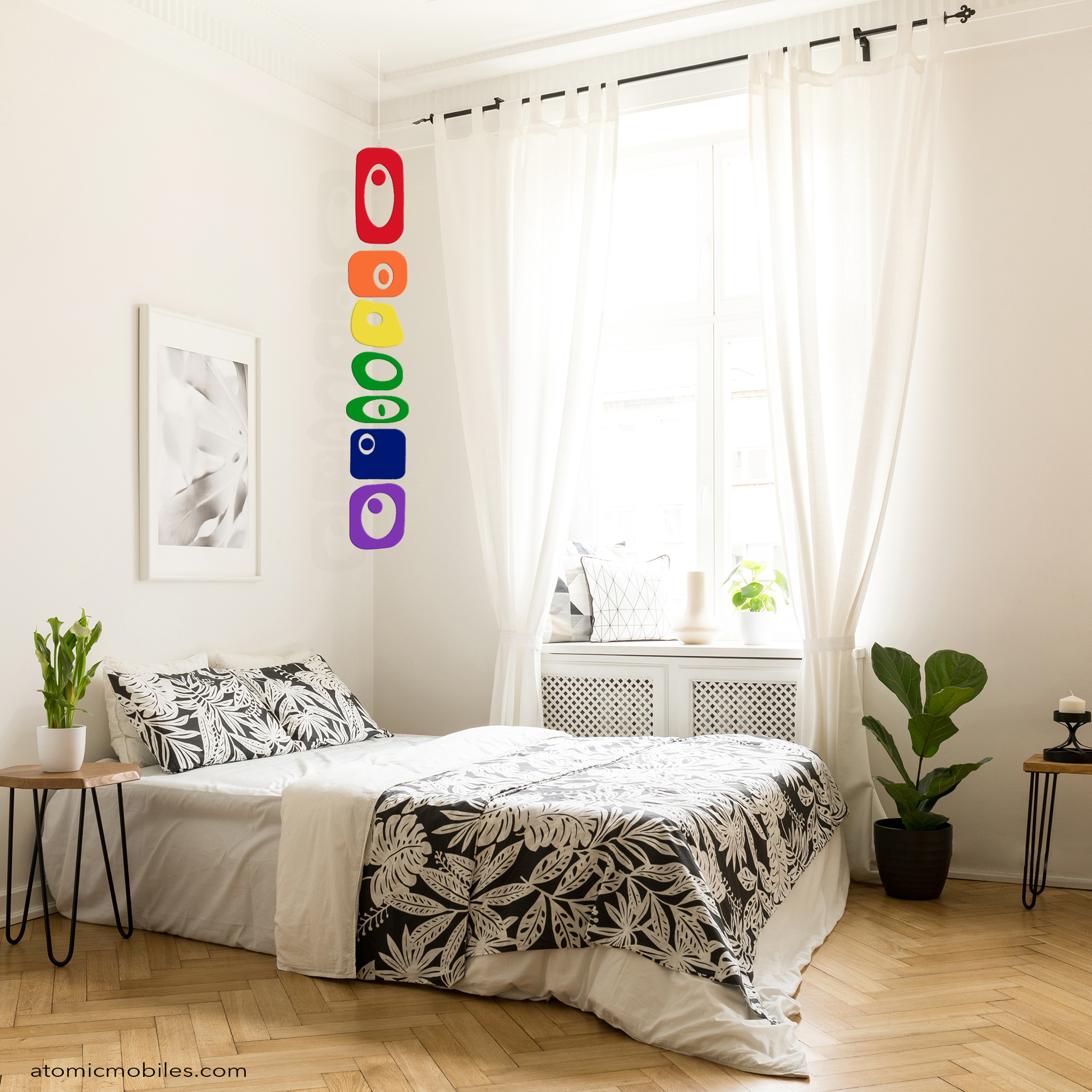 Beautiful urban bedroom with tall ceiling, large drapes, parque floor, with Beatnik Party LGBTQ+ Rainbow Pride vertical hanging art mobile by AtomicMobiles.com