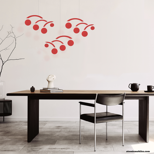 3 transparent red acrylic modern hanging art mobiles by Atomic Mobiles in contemporary dining room with wood table 