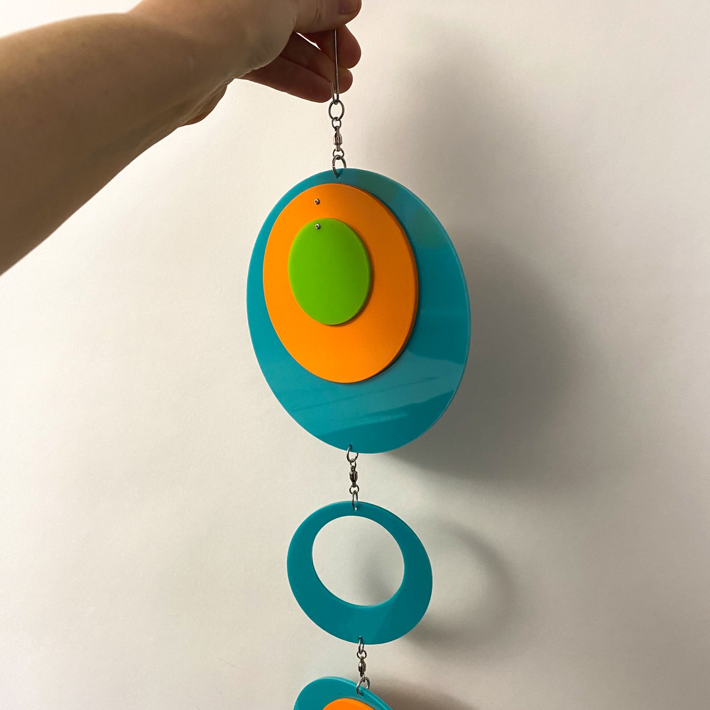 Holding the beautiful Palm Springs Wall Art Mobile in Aqua Blue, Orange, and Lime Green by AtomicMobiles.com