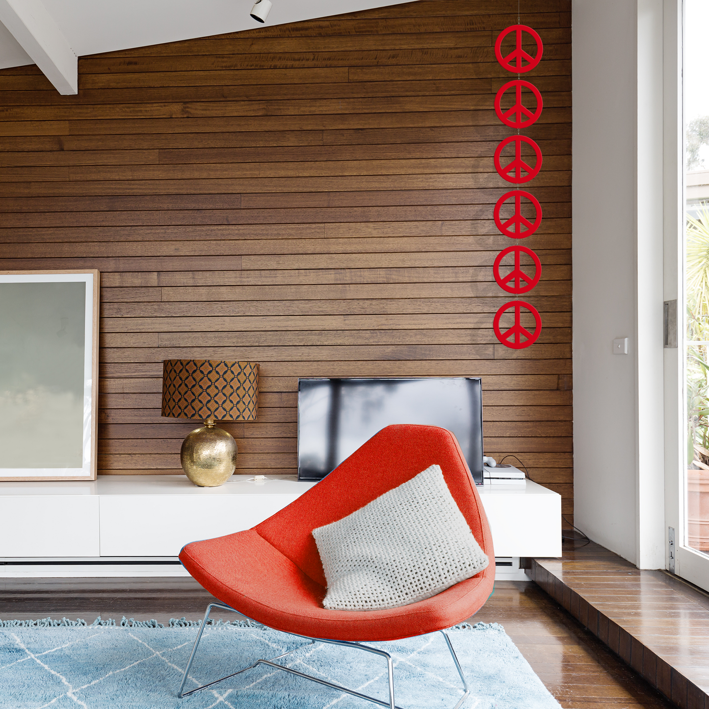 Modern living room with wood paneled wall and mid century modern red chair with Peace Mobile - hanging kinetic art mobile in red by AtomicMobiles.com